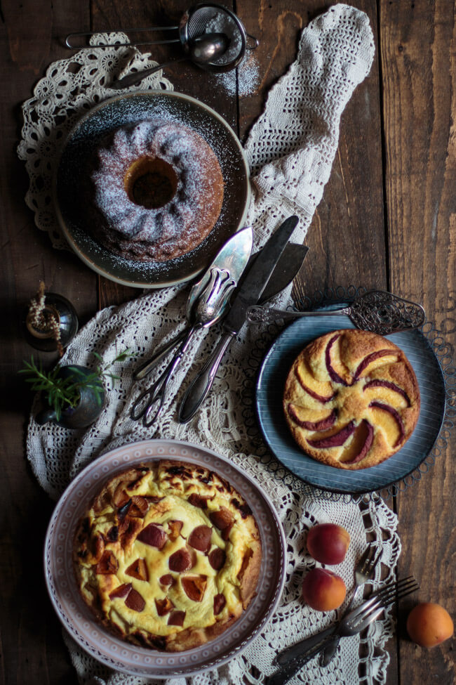 Drei Kuchen auf dunklem Holztisch mit Eierlikör, Aprikosen und Pfrisichen