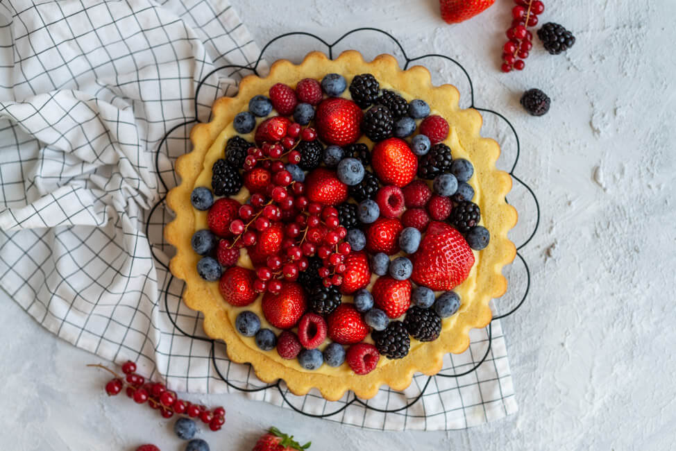 Obstkuchen mit Erdbeeren, Himbeeren, Heidelbeeren, Johsannisbeeren und Brombeeren und Eierlikörpudding auf schwarzem Tortengitter. #Bisquit #Obstkuchenboden #Eierlikörpudding
