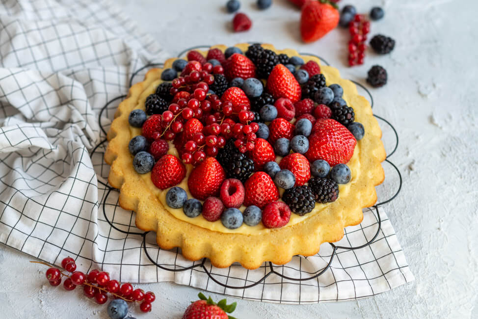 Obstkuchen mit Erdbeeren, Himbeeren, Heidelbeeren, Johsannisbeeren und Brombeeren und Eierlikörpudding auf schwarzem Tortengitter. #Erdbeerkuchen #Beerenkuchen #Sommer #Dessert