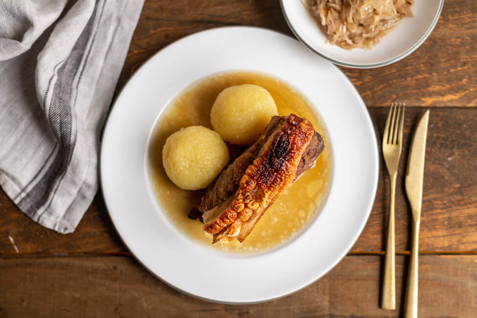 Fränkisches Schäufele mit Sauerkraut und Kloß auf weißem Teller und rustikalem Holztisch.