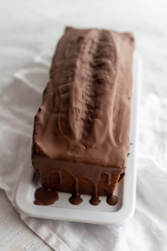 Einfacher Schokoladenkuchen mit Schokoladenglasur auf weißer Kuchenplatte.