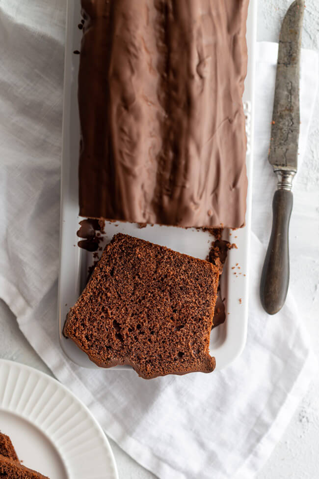 Einfacher Schokoladenkuchen mit Schokoladenglasur auf weißer Kuchenplatte.