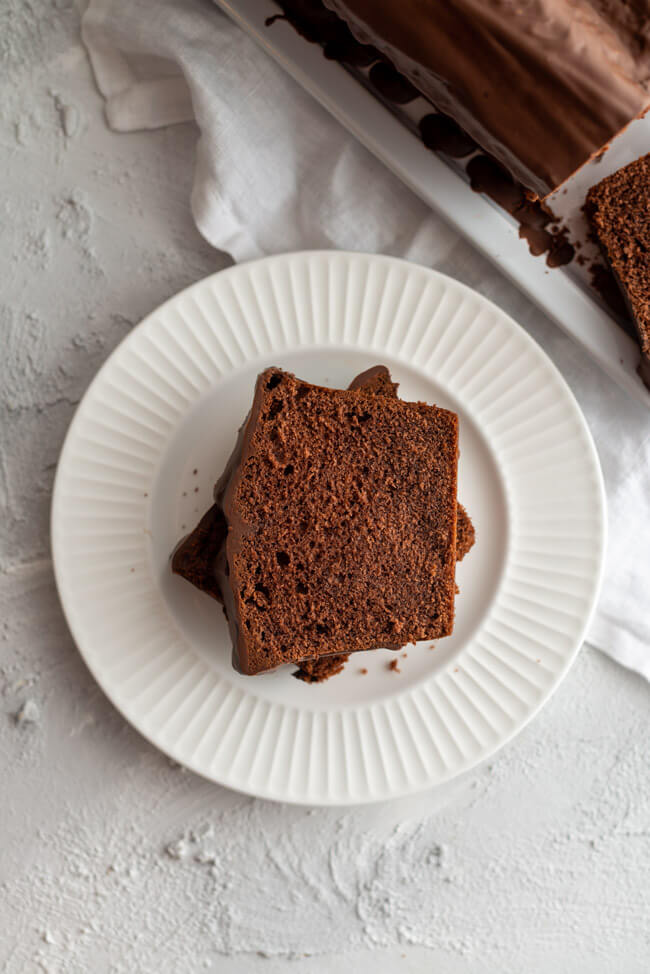 Zwei Stücke vom einfachen Schokoladenkuchen mit Schokoladenglasur auf weißer Kuchenplatte.