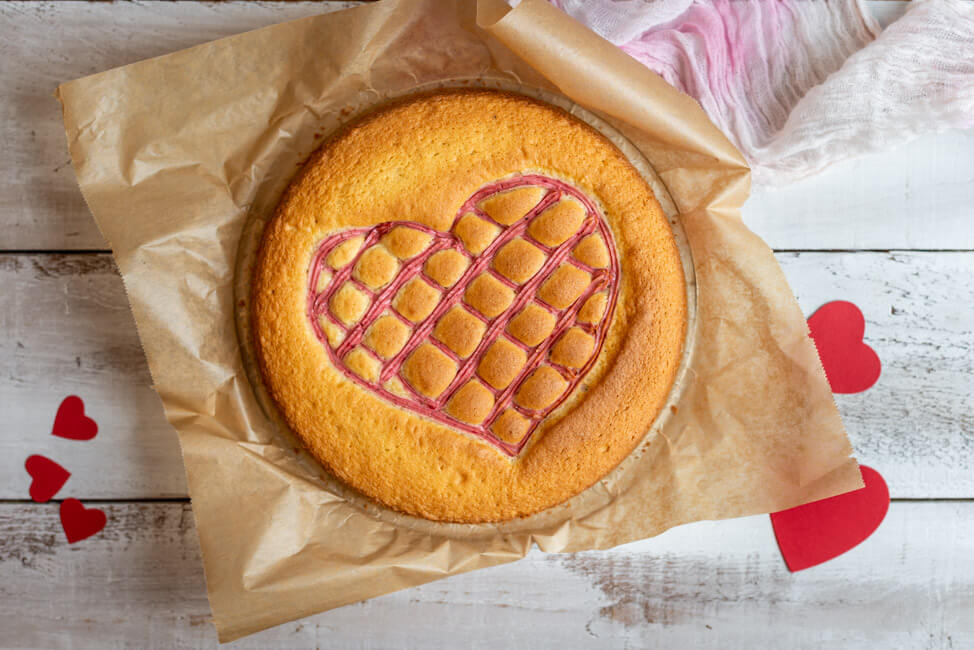Steppdeckenkuchen für den 14.02.: Herzkuchen zum Valentinstag mit Erdbeerquark auf weißem Holzbrett.