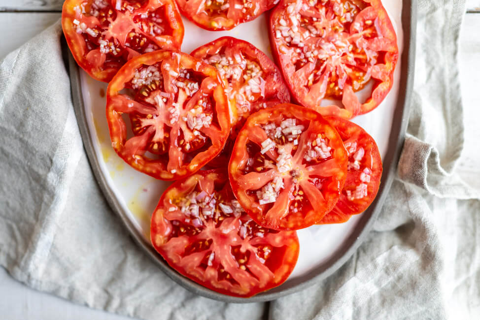 Einfacher Tomatensalat, aus Ochsenherztomaten mit Zwiebel-Vinaigrette, auf weißem Keramikteller.