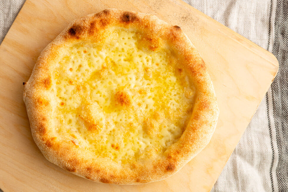 Weiße Pizza mit Emmentaler und Mozzarella auf Holzbrett