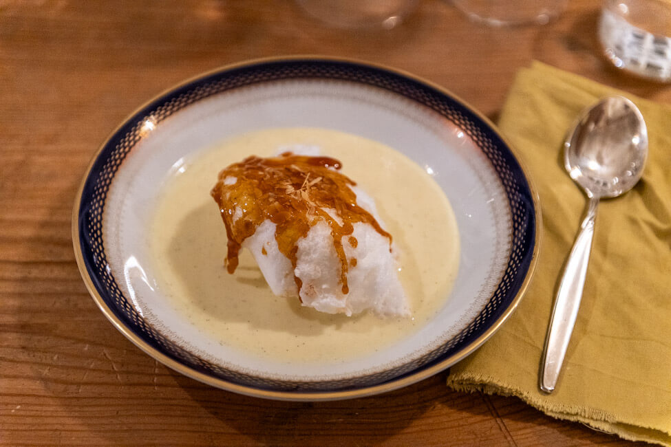 Schneeeier mit Mandelkrokrant auf Vanillesauce, serviert auf Porzellanteller mit Goldrand.
