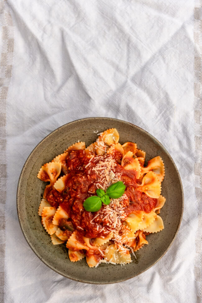 Ein Teller Farfalle mit Tomatensauce mit Thunfisch und Auberginen auf weißem Untergrund.