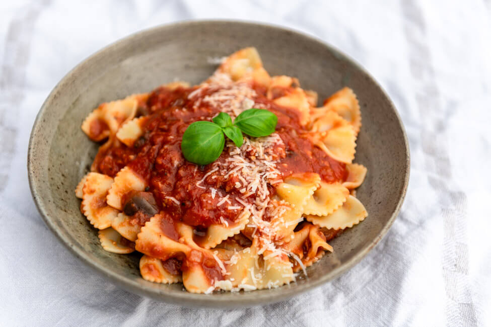 Ein Teller Farfalle mit Tomatensauce mit Thunfisch und Auberginen auf weißem Untergrund.