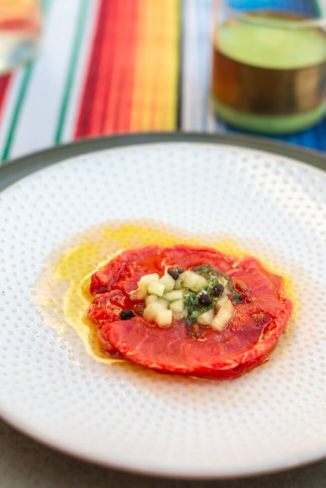 Wassermelonen Carpaccio mit fermentiertem Kampot Pfeffer auf hellem Teller und bunter Tischdecke.