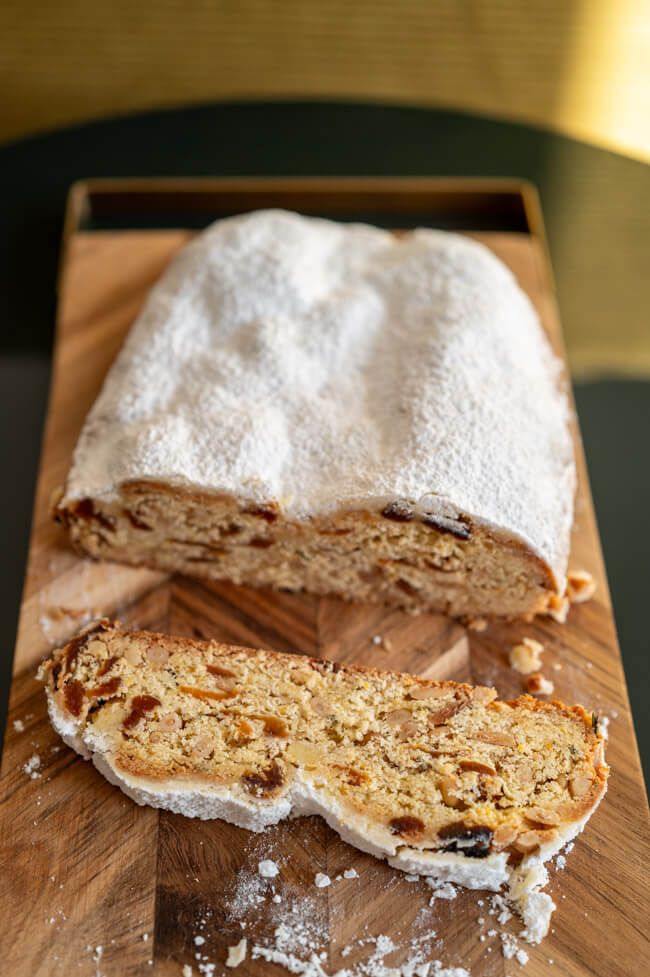 Ein Stück Aprikosen-Stollen mit Pinienkernen und Rosmarin auf Holzbrett aufgeschnitten.